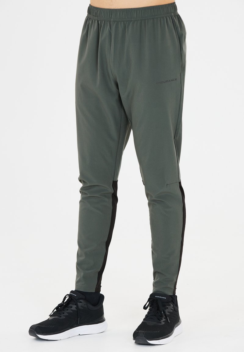 Mäns träningsbyxor i mörkgrön, tillverkade av lättviktig tyg med elastisk midja och svarta accentpartier på sidorna. Kombineras med svarta sneakers.