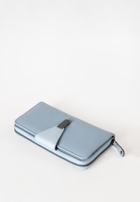Lichtblauwe portemonnee van gestructureerd leer, met een contrasterende flap van glad leer en een zwarte rits, met een compacte rechthoekige vorm.