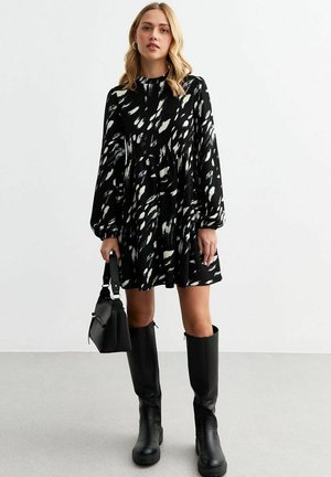 Black dress with white abstract pattern, long balloon sleeves, and a fitted waist. Paired with knee-high black boots and a small black handbag.