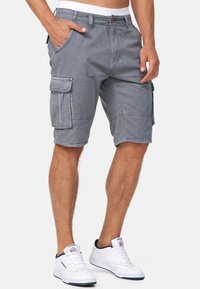 Grå cargo shorts med flere lommer, lavet af blødt stof. Har en afslappet pasform og lukning med knap i taljen. Stylet med hvide sneakers.