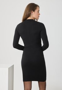 Fekete, hosszú ujjú, testhez simuló ruha, térdhosszúságú, puha anyagból készült. Kerek nyakkivágással és varrás nélküli kialakítással rendelkezik. Finom hátoldali részletezéssel.