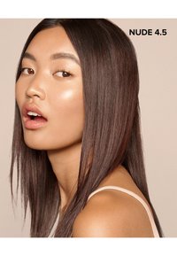Producto cosmético etiquetado como "NUDE 4.5". Modelo con cabello largo y castaño, piel suave y color de labios neutro. Fondo minimalista.
