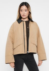 Beige, ylipainoinen takki mustalla kauluksella. Varustettu vetoketju edessä, leveillä hihoilla ja kahdella etutaskulla. Valmistettu sileästä, teksturoidusta kankaasta.