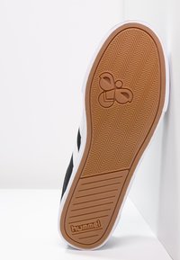 Fekete sneaker talp, halászmintával, fehér középtalppal és gumírozott barna külső talppal, amelyen a hummel logo és dizájn kiegészítők találhatók.