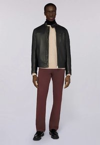 Černá kožená bunda s vysokým límcem, béžový svetr pod ní, vínové kalhoty a černé mokasíny. Hladká textura a pouzdrový střih.