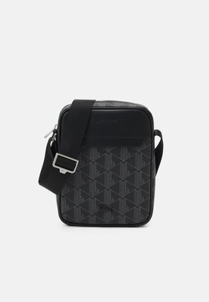 Sac bandoulière noir avec un motif géométrique, des accents lisses et une sangle réglable. Comprend une fermeture zippée et des détails de marque.
