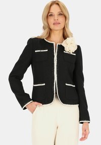 Czarna kurtka z białymi wykończeniami, okrągłym dekoltem, przednimi kieszeniami i materiałowym kwiatem na ramieniu. Strukturalny, tkany materiał.