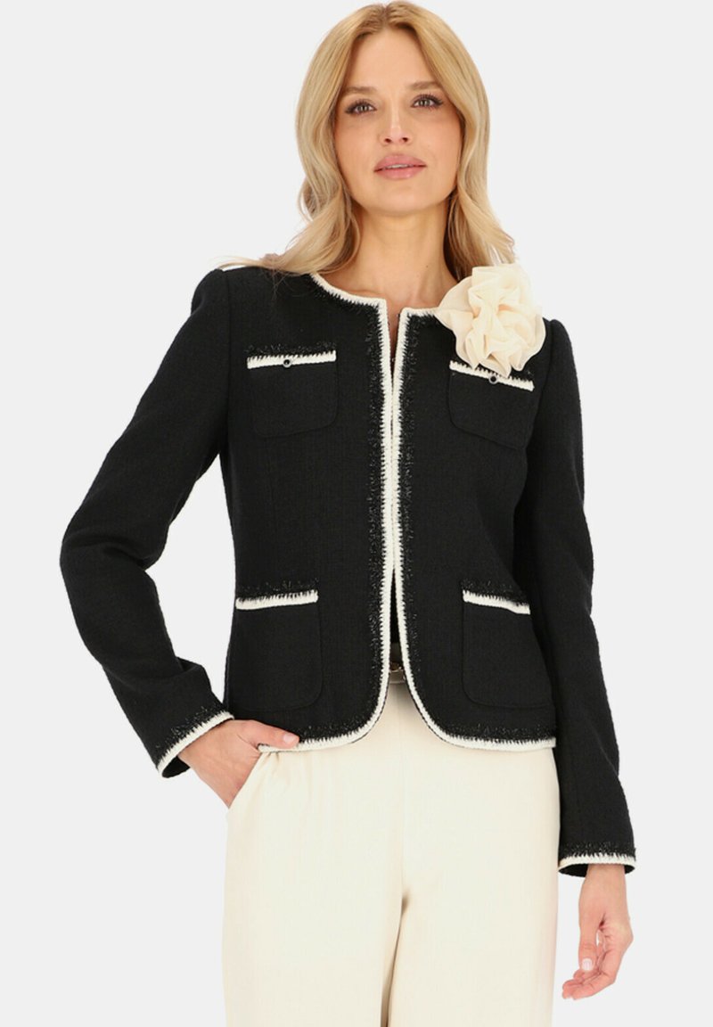 Czarna kurtka z białymi wykończeniami, okrągłym dekoltem, przednimi kieszeniami i materiałowym kwiatem na ramieniu. Strukturalny, tkany materiał.