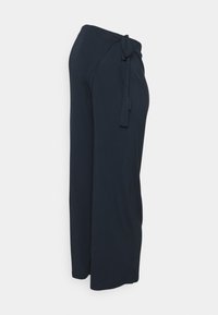 Tmavě modré kalhoty širokého střihu vyrobené z měkké látky, s detaily vázaného pasu. Hladký povrch a žádné viditelné vzory.