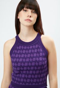 Top morado sin mangas con un patrón texturizado, que presenta un escote redondo y acentos acanalados. El material parece suave y elástico.