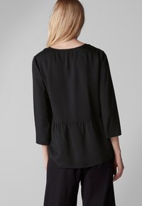 Schwarzes Oberteil mit drei Viertelärmeln und einem gerafften Peplumsaum. Glattes Material mit einem lockeren Schnitt und weitem Ausschnitt.