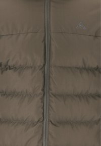 Brun puffjacka med en texturerad yta, framtida dragkedja och en liten logotyp. Har quiltade sektioner för isolering och form.