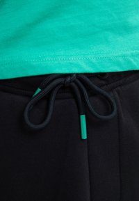 Grøn bomulds t-shirt parret med sorte pants med snoretræk. Snoretrækkene har grønne spidser, med en blød tekstur og elastisk talje.