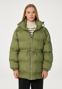 Groene pufferjack met een cinch taille, volledige ritssluiting, hoge kraag en ribgebreide mouwen. Heeft een gladde, glanzende textuur en subtiele stikdetails.