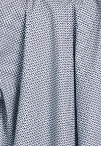 Lichtblauwe stof met een herhalend geometrisch patroon van cirkels in marineblauw en beige. Zachte textuur, geschikt voor kleding of textiel voor in huis.