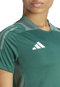 Maglia sportiva verde a maniche corte, con collo rotondo, leggero effetto texture e logo bianco adidas sul petto e sulle strisce delle spalle.