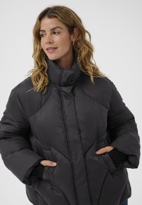 Černá péřová bunda s vysokým límcem, texturovanými panely a bočními kapsami. Obsahuje silnou izolaci a měkkou tkaninu pro teplo.