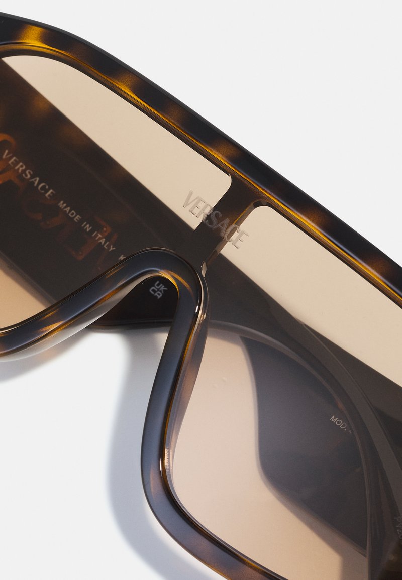 Versace zonnebril met een schildpaddenframe, bruin gradient glazen en gegraveerd logo. Heeft een dikke, ronde vorm en een soepele textuur.
