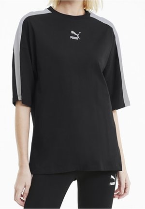 Kobieta nosząca czarny oversize T-shirt Puma z szarymi paskami na rękawach oraz pasujące czarne legginsy Puma.