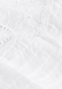 Hvidt stof med indviklet broderi og delikat stribet tekstur. Materialet er blødt, med lagdelt syning og en subtil glans.