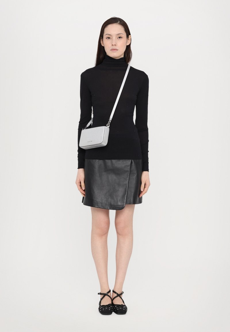 Top a collo dell'uccello nero, aderente; gonna avvolgente in pelle nera; borsa crossbody argento; scarpe basse nere con cinturini incrociati e pois bianchi.