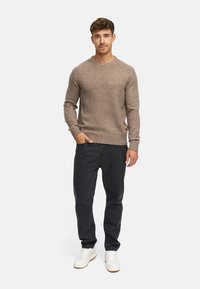 Lys brun strikket trøje med rund hals, parret med mørk denim jeans og hvide sneakers. Simpelt design, blød tekstur og tætsiddende form.