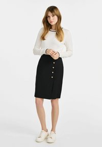 Czarna spódnica ołówkowa z klamrą, ozdobiona pięcioma złotymi guzikami z przodu. Biała bluzka z długim rękawem z czarnymi wykończeniami i casualowe sneakersy.