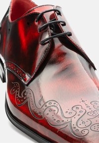 Glänzender roter Leder-Schuh mit schwarzen Schnürsenkeln, verziert mit einem filigranen Oktopus-Muster, das seitlich eingraviert ist, sowie dekorativen perforierten Details.