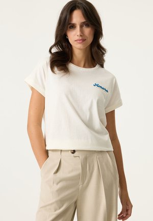 Witte katoenen T-shirt met opgerolde mouwen, met blauwe geborduurde tekst "Amore". Gecombineerd met beige op maat gemaakte broek.