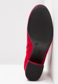 Chaussure en daim rouge avec une semelle texturée noire et un talon bloc reposant sur une surface blanche, affichant la marque "Gabor" et la taille 4½ sur la semelle.