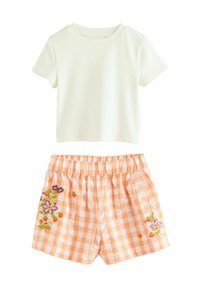 Kortærmet ribbet skjorte i creme, parret med ferskenfarvede ternede shorts med blomsterbroderi og elastisk talje.