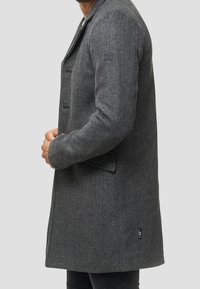 Manteau gris en mélange de laine avec col, design à simple boutonnage, poches avant et tissu texturé. Comprend un petit logo sur la manche.