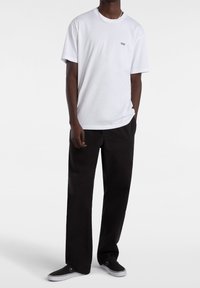 White short-sleeve T-shirt with a small black "Vans" logo on the chest, paired with loose-fitting black pants and black sneakers.