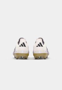 White soccer cleats with black accents, textured upper, low-profile design, and transparent studs. Rear view shows three stripes logo.