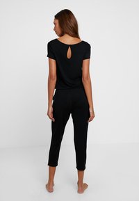 Zwart tweedelig outfit met een top met korte mouwen en een keyhole aan de achterkant, en een cropped broek, gemaakt van zachte, elastische stof.