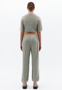 Tvådelat set bestående av en ljus olivgrön cropped topp och matchande löst sittande byxor. Tyget ser mjukt ut med en lätt lyster och elastisk midja.