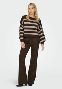 Un pull rayé brun et crème avec un large encolure et des manches bouffantes, associé à un pantalon évasé brun et des bottes à talons noires.