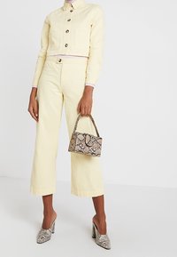 Žlutá zkrácená džínová bunda a odpovídající široké kalhoty, doplněné malou kabelkou s hadím potiskem a vzorovanými lodičkami na podpatku.