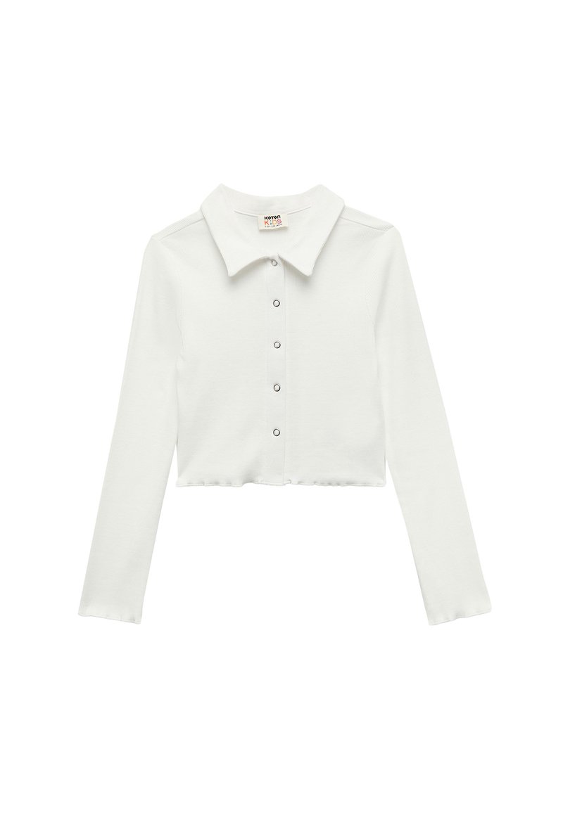 Camicia bianca cropped a maniche lunghe con colletto e chiusura frontale a bottoni. Realizzata in un materiale morbido e testurizzato. Presenta un orlo dritto.
