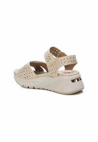 Sandalias perforadas beige con doble tirante, plantilla acolchada y suela de cuña blanca con un acento metálico en el talón.