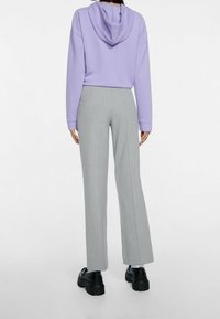 Fialová mikina s kapucí se uvolněným střihem a žebrovanými manžetami, doplněná světlými šedými kalhotami s jemným proužkem a robustními černými platformovými botami.