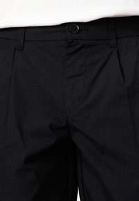 Pantalon noir en matériau léger avec une taille plate, une fermeture à bouton et des poches. Texture lisse avec des coutures minimales visibles.