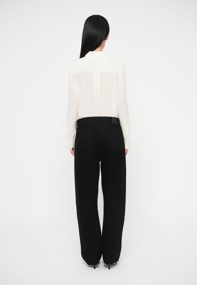 Balta, caurspīdīga blūze ar apkakli un aizmugures plecu daļu; kombinēta ar melnām, platiem biksēm. Gluda tekstūra, minimālas detaļas, elegants piegriezums.