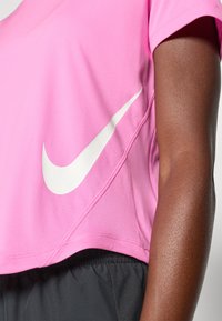 Rosa Nike cropped t-skjorte med en hvit logo på siden. Laget av myk, pustende stoff med en jevn tekstur og korte ermer.