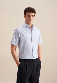 Camicia a maniche corte con bottoni, a strisce verticali blu chiaro e bianche, realizzata in un tessuto morbido, con colletto a punta e design aderente.