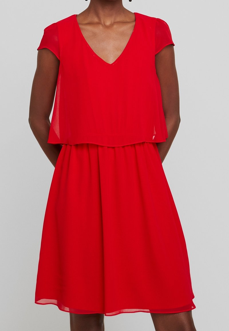 Robe en chiffon rouge avec un décolleté en V, des manches courtes et un corsage à couches. Jupe évasée avec une texture lisse, longueur au genou.