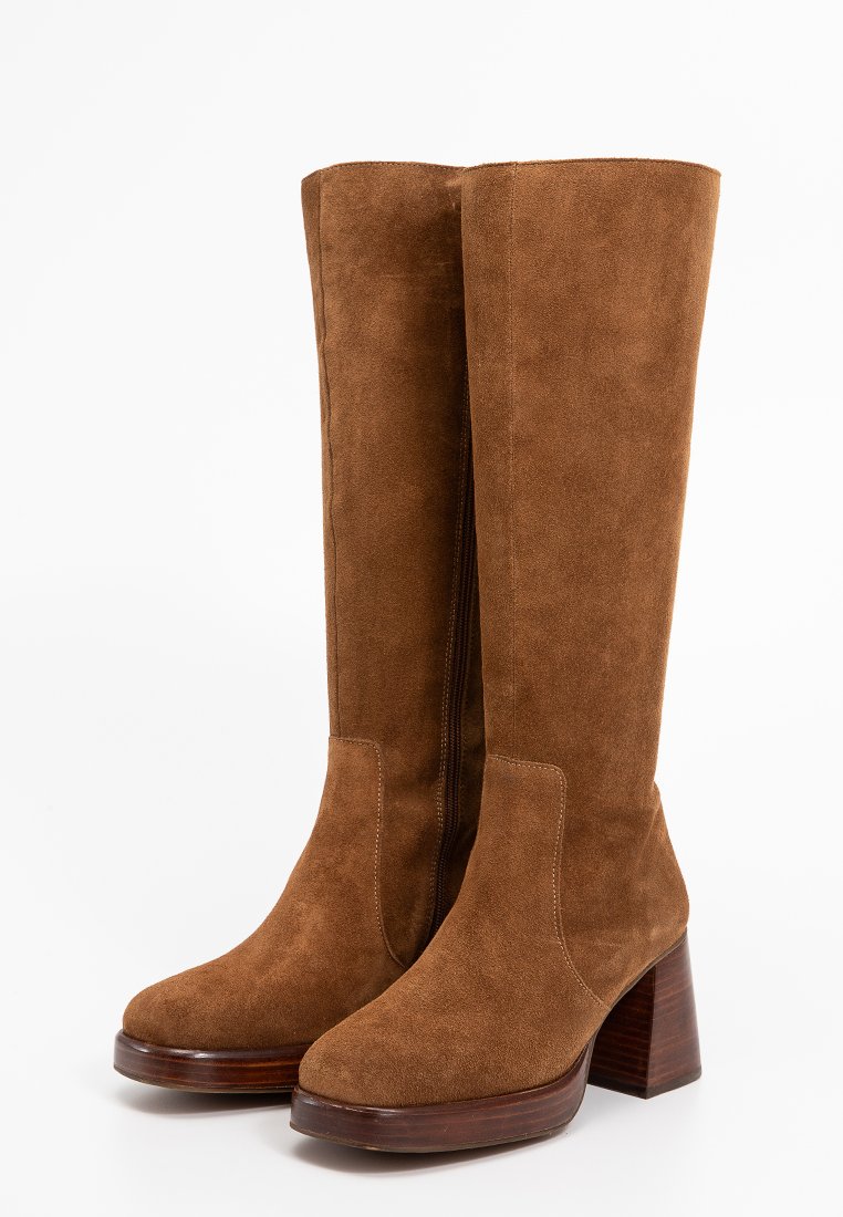 Bottes en daim marron jusqu'au genou avec un talon bloc et un bout arrondi. Dotées d'une fermeture éclair sur le côté et de coutures ton sur ton pour les détails.