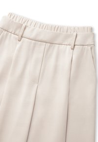 Beige broek met een geplooid front en een elastische tailleband. De stof heeft een gladde textuur en subtiele diagonale lijnen.