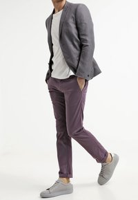 Szary lniany żakiet, biały T-shirt, purpurowe chinosy i szare trampki. Żakiet ma jeden guzik, dopasowany krój oraz otwarte kieszenie.