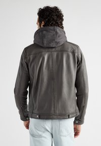 Donkergrijze leren jas met een grijze stoffen capuchon. Kenmerkt zich door een slim fit ontwerp, schoudernaden en ritsmanchetten. Zacht textuur en een strakke uitstraling.